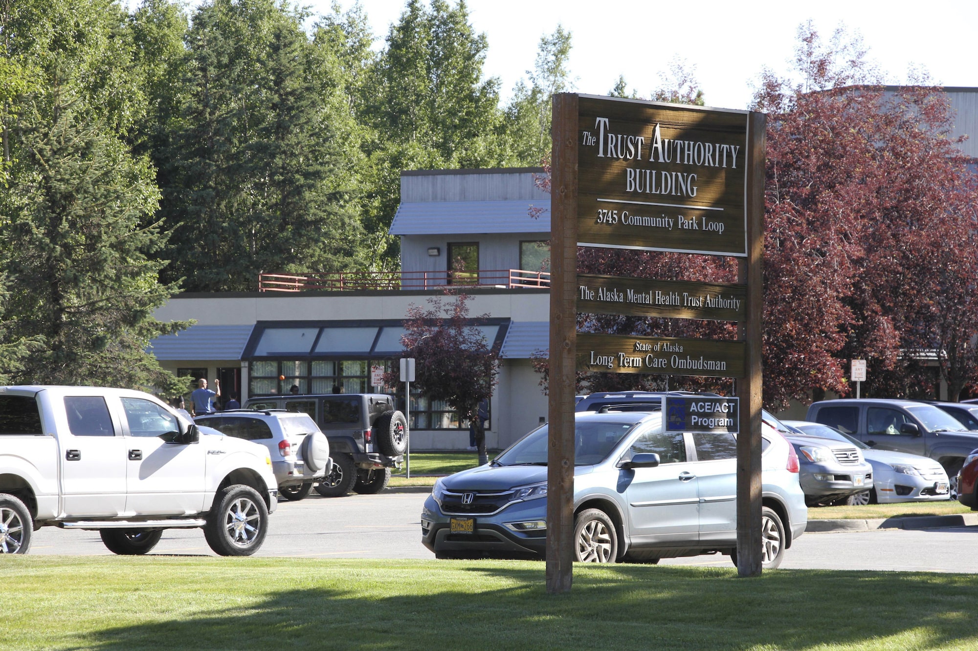 a brown sign reads the Trust Authority Building outside an office building near cars and trees