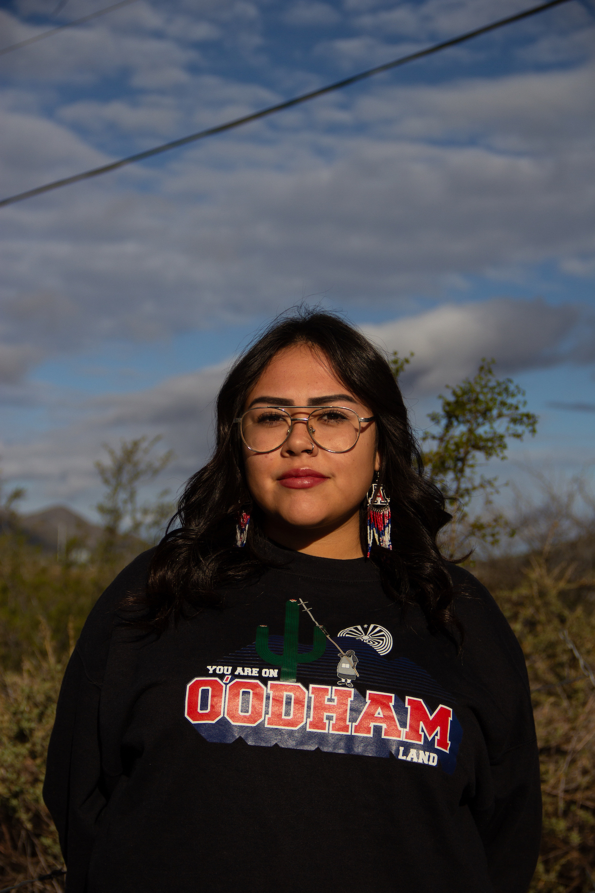 A woman in a black sweatshirt looks directly into the camera