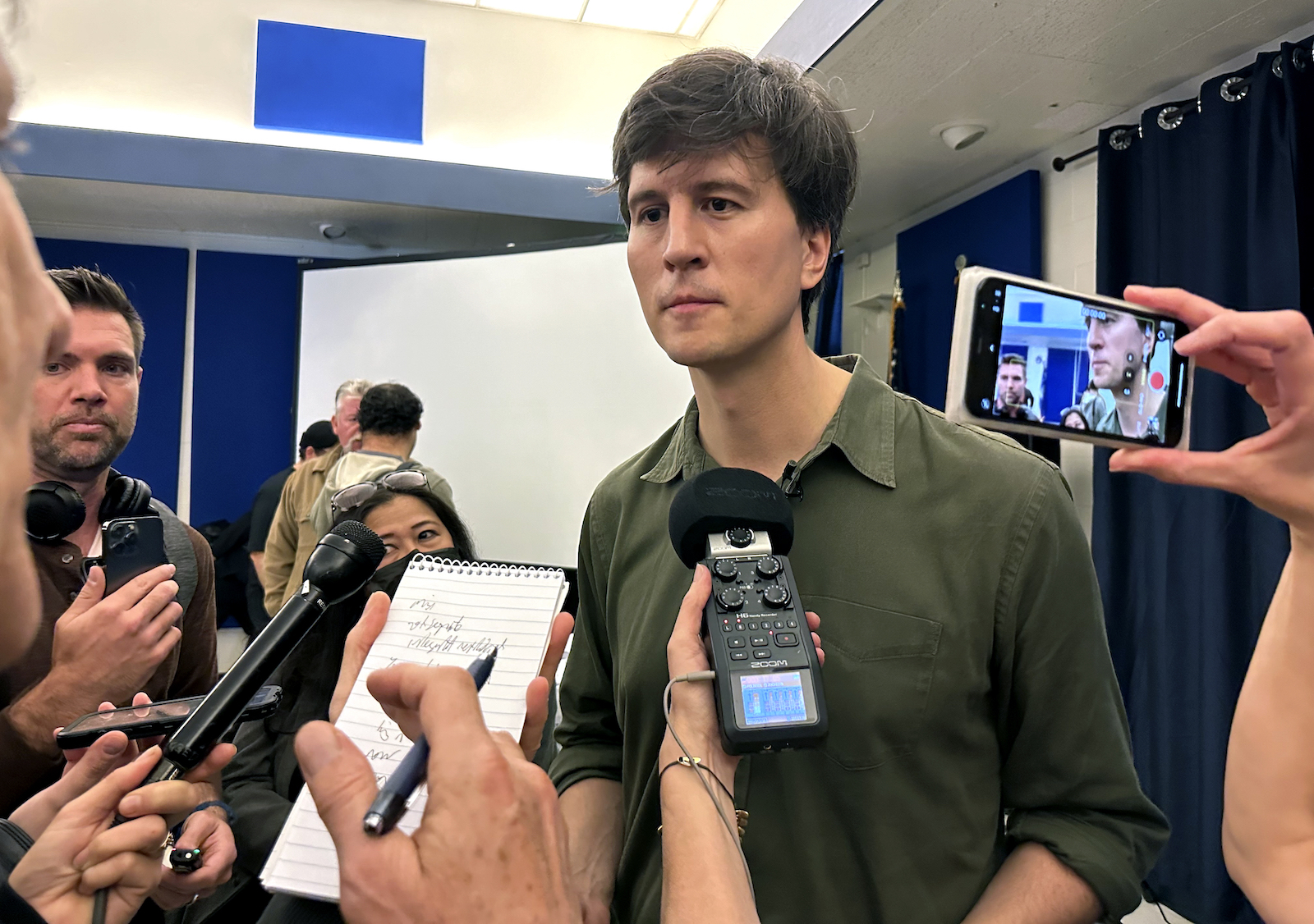 reporters hold up microphones to a man who is not smiling